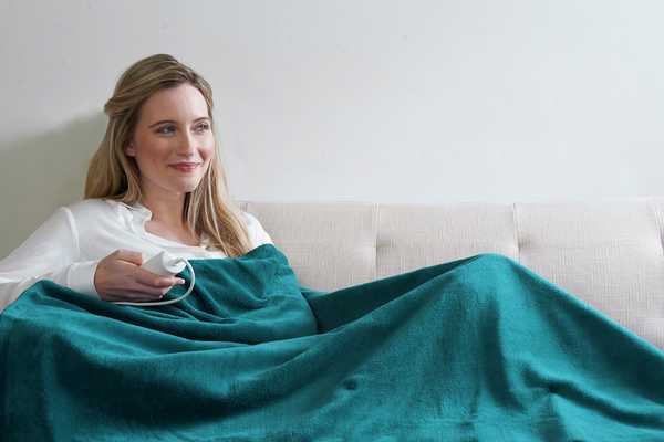 Woman cosying up on a sofa with an electric blanket.